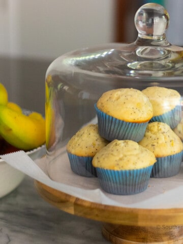 Muffins stacked on a cake plate with a glass dome.